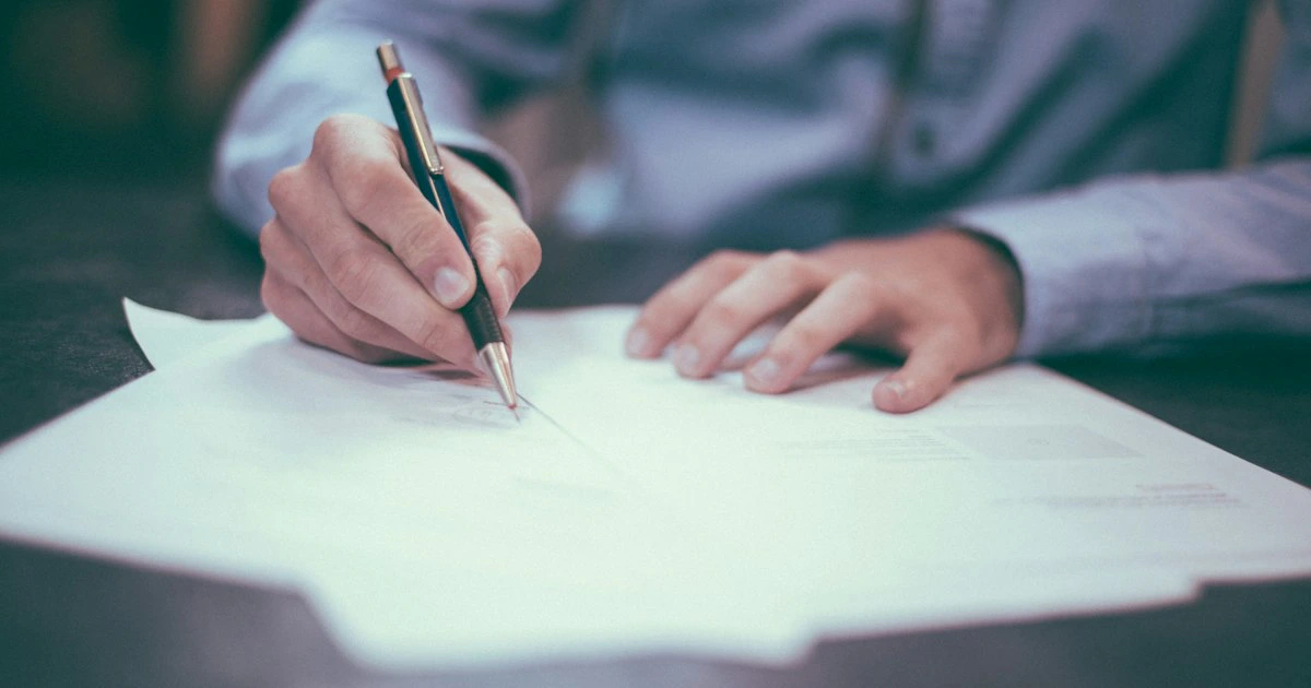 Two professionals reviewing and signing business documents at a desk